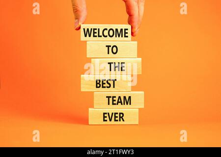 Welcome to best team symbol. Concept words Welcome to the best team ever on wooden block. Beautiful orange table background. Businessman hand. Busines Stock Photo