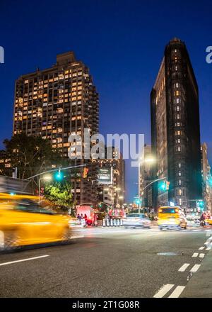 New York City, New York - October 12, 2023: Midtown Manhattan street scene with the historic Flatiron Building, cars and people at night. Stock Photo