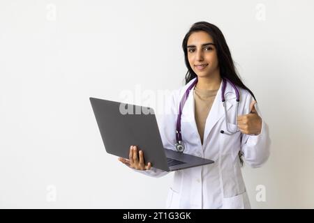 Cheerful young attractive hindu woman medical worker in uniform works at computer isolated on white background. Social distance during covid-19 pandem Stock Photo