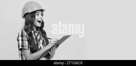 Renovation child, surprised teen girl in construction helmet making notes in clipboard, check results. Child builder in helmet horizontal poster desig Stock Photo