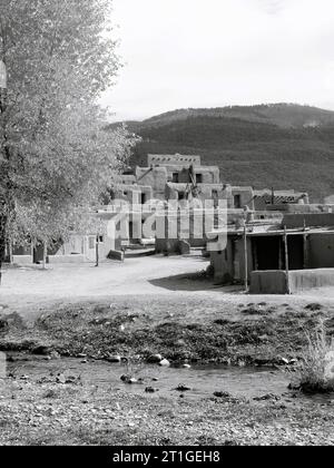 Monochrome autumn with Taos Pueblo stream, tree, and community buildings Stock Photo