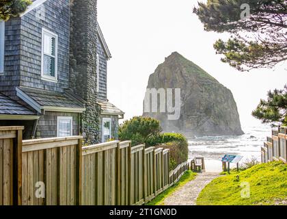 A pathway to the beach and Haystack Rock goes past a  clapboard beach house in Cannon Beach, Oregon, USA. Stock Photo