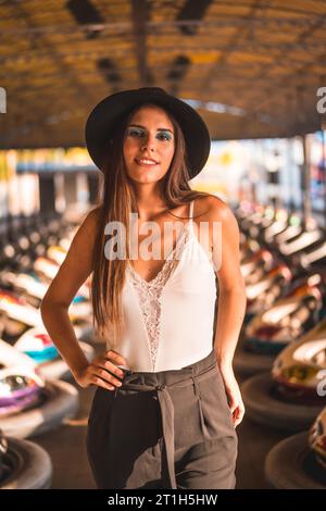 Lifestyle, portrait of a brunette Caucasian with heels, pants and black hat in an amusement park in the bumper cars Stock Photo