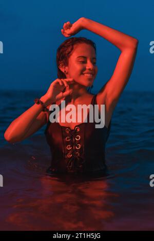 Lifestyle of a young pretty brunette Caucasian bathing at night in the sea with an illuminated red light, vertical photo Stock Photo