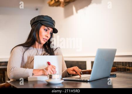 Latina brunette architect taking notes in online meeting from a coffee shop Stock Photo