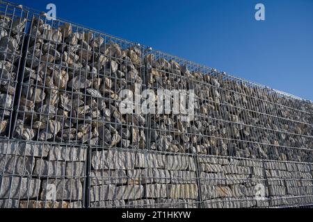 Gabion fence made of steel bars filled with gray granite stone. Blue sky. Copy space.up view. Stock Photo