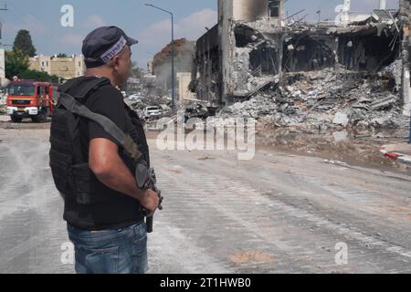 An armed police officer stands next to the police station that was destroyed after a battle between Israeli troops and Hamas militants that have take the station on October 8, 2023 in Sderot, Israel. On Saturday, the Palestinian militant group Hamas launched the largest surprise attack from Gaza in a generation, sending thousands of missiles and an unknown number of fighters by land, who shot and kidnapped Israelis in communities near the Gaza border. Stock Photo