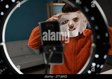 Man making a video for his blog on cosmetics using a smartphone and ring lamp. Male blogger review product on camera. Stock Photo