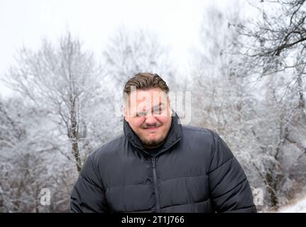 Young man in a thick winter jacket looking mischievously into the camera with one eye closed Stock Photo