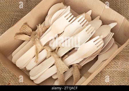 Wooden cutlery, tied with hessian jute fabric, in a cardboard tray on hessian fabric. Eco friendly biodegradeable recycling plastic free takeaway Stock Photo