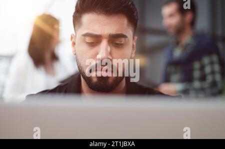 Seriously focused determined young bearded businessman or freelancer sitting at the table, Stock Photo