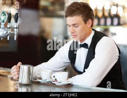 Coffee, barista and young man waiter in cafe making a latte, espresso or cappuccino at an event. Hospitality, server and male butler preparing a warm Stock Photo