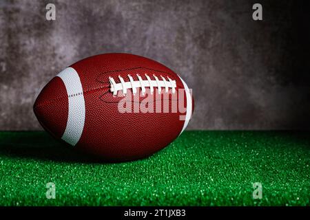 An american football ball over a ground with green grass in front of a concrete wall. Stock Photo