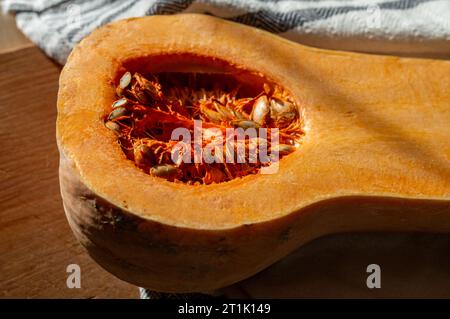 halved pumpkin, with pumpkin seeds, on a cutting board and kitchen towel Stock Photo