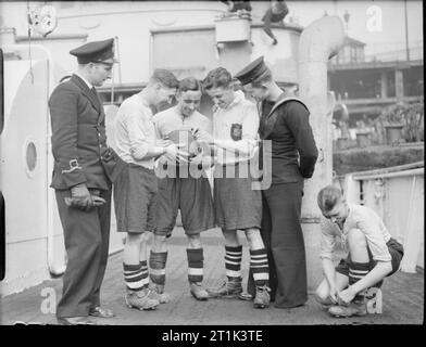 The Royal Navy during the Second World War Four members of HMT MAN O'WAR's football team wearing their kit as they get ready for their next conquest on board ship at Liverpool. Two other members of crew are with the men. The football team composed of members of the crew of the trawler holds the record of their base, twenty games played, nineteen won, and one drawn. Despite the discomforts of life on board at sea in their tiny ship, the crew when in harbour take on opposite teams from other ships - and win - this being their idea of resting. Stock Photo