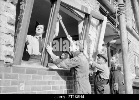 Royal Air Force Coastal Command, 1939-1945. Airmen from No. 24 Air Sea Rescue Unit assist civilian workers to renovate bomb-damaged council houses at Gorleston-on-Sea, Norfolk. Leading Aircraftman Lawrence Keegan (1st left) and Aircraftman Arthur Ainscough (3rd left), fitting a window under the supervision of Mr A J Underwood (far right), were taking part in an ambitious Educational and Vocational Training programme to provide airmen with practical training for civilian life by loaning them out to local businesses. Stock Photo