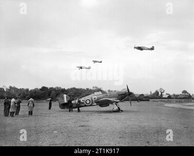 Royal Air Force Fighter Command, 1939-1945. Journalists from Dominions newspapers watch a flight of Hawker Hurricane Mark Is of No. 56 Squadron RAF taking off for a sortie over France from North Weald, Essex. In the foreground another Hurricane Mark I of the Squadron, P2764 'US-P', stands at its dispersal point near the perimeter track on the south-western edge of the airfield. Stock Photo