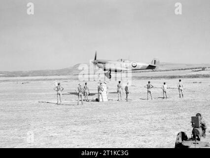 Royal Air Force- Italy, the Balkans and South-east Europe, 1942-1945. Ground personnel watch as Supermarine Spitfire Mark IX ('UF-?') of No. 601 Squadron RAF, comes in to land land on the newly-completed airfield at Lentini West, Sicily. Four Spitfire squadrons of No. 244 Wing RAF were operating from the airfield by the following day. Stock Photo
