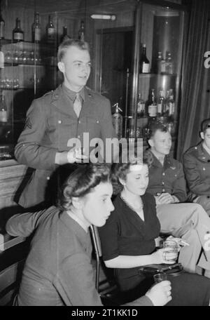 Empire - and World - Party- Radio Broadcast From the Overseas Club, St James's London, 1942 A group of two Americans and two Britons listen to the broadcast from the Hall of India at the Overseas Club. Left to right they are: ACW2 Patricia Graham WAAF (from, Ripley, Hampshire), Corporal H Bielski (standing, from Rapid City, South Dakota), ACW2 Maclean WAAF (was in Tangier until 4 years ago), and Lieutenant Peyton Mathias (from Montgomery, Alabama). Stock Photo