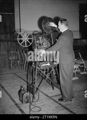 Film Show at Highest Village in the Highlands- Ministry of Information Film Screening, Tomintoul, Banffshire, Scotland, UK, 1943 Ministry of Information Film Operator John Macdougall sets up his Bell and Howell film projector in the Memorial Hall, Tomintoul. The hall is being converted into a cinema for the evening, and just visible are the rows of chairs which have been set up to accommodate the audience. The film is due to begin at 8pm. Stock Photo