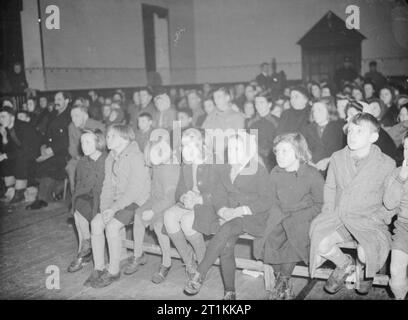 Film Show at Highest Village in the Highlands- Ministry of Information Film Screening, Tomintoul, Banffshire, Scotland, UK, 1943 Children sit on benches in the front row to watch a Ministry of Information film being shown in the village hall in Tomintoul, Scotland. The original caption states that the 'pictures shown are a mixed bag - documentaries, play films, news'. All members of the audience are wearing coats as there is no heating in the hall. Stock Photo