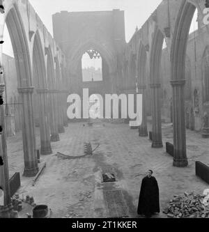 A Church Rises From the Ashes- Bomb Damage To St George's Cathedral, Southwark, 1942 A priest, probably Father Dixon, stands in the roofless shell of St George's Roman Catholic Cathedral, on the corner of St George's Road and Lambeth Road in Southwark, South East London. The Cathedral was severely damaged by an incendiary bomb attack which gutted the building on 16 April 1941. The photograph is taken from the altar end of the building, looking back down the nave towards the door. Stock Photo
