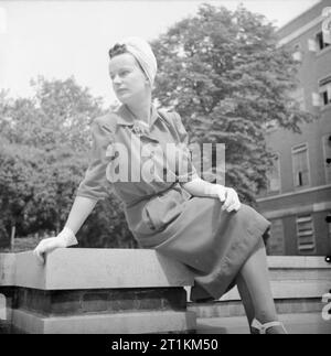 How a British Woman Dresses in Wartime- Utility Clothing in Britain, 1943 A  model sits on a plinth beside some steps to show off her scarlet wool  Utility frock by Dorville at John Lewis and Co. Ltd., with front-gathered  skirt and shirt-waist top (cost: 11 coupons ...