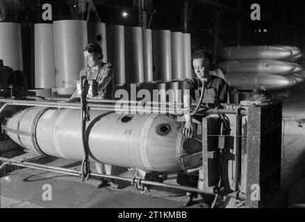 Jettison Petrol Tanks- the Production of Jettison Tanks For USE by the United States Army Air Force and Royal Air Force, Britain, 1944 At a factory producing jettison petrol tanks for the American and Royal air forces, somewhere in Britain, Miss Ethel Prett (left) and Miss Nellie Robery work at a large press which forces the two spigotted ends onto the body of the tank. Behind them, a large stack of tanks can be seen. Stock Photo