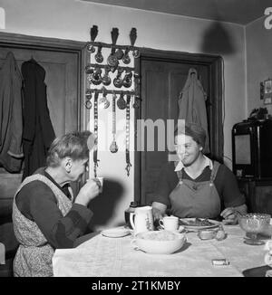 Landgirl's Day- Everyday Life and Agriculture in West Sussex, England, UK, 1944 At twelve o'clock, 19 year old Land Girl Rosalind Cox pauses in her day's work and returns to her billet for lunch. Her landlady, Mrs Annie Weaver, enjoys a cup of tea whilst Rosalind tucks into a large plate of rabbit stew. Behind them on the wall, is a display of horse brasses, won by Mrs Weaver's husband. Stock Photo