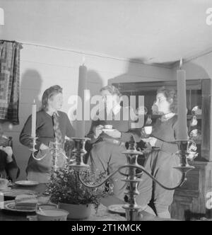 Landgirl's Day- Everyday Life and Agriculture in West Sussex, England, UK, 1944 29 year old Land Girl Rosalind Cox (centre) and her colleagues enjoy an evening of coffee, sandwiches and gossip in the candle-lit interior of 400 year old Prattendens Cottage in Bury, West Sussex. The cottage was occupied by the radio star Mabel Constanduros before the war. These get-togethers occur every Monday evening, giving the Land Girls the opportunity to relax and talk to one another. Stock Photo