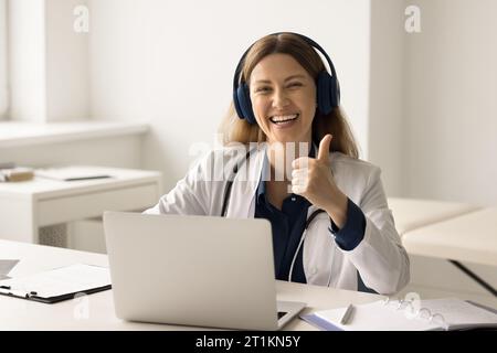 Portrait of happy medical worker in headphones showing thumb up Stock Photo