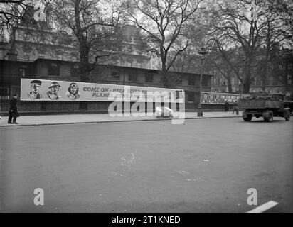 Ministry of Information Campaign Posters, London, UK, 1941 A view of a poster site in London, showing two long posters. The first, on the left of the photograph, shows a sailor, soldier and airman each giving the thumbs up sign with the caption 'come on - help build us planes, guns and ships - mobilise for war work'. The second poster, just visible on the right, features the same three men, but they are pointing, and the beginning of the caption reads 'you can help build us...'. Stock Photo