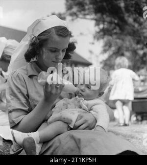 Nursery For Working Mothers- the work of Flint Green Road Nursery, Birmingham, 1942 A young nurse bottle feeds a baby in the evening sunshine in the grounds of Flint Green Road Nursery. Stock Photo