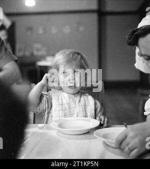Nursery For Working Mothers- the work of Flint Green Road Nursery, Birmingham, 1942 A young girl finishes her last spoonful of porridge at Flint Green Road Nursery. The rest of her breakfast will consist of bread and butter and a large mug of milk. Stock Photo