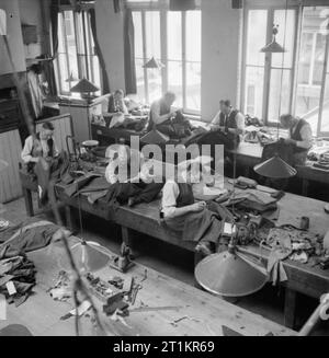 Savile Row- Tailoring at Henry Poole and Co., London, England, UK, 1944 A view of the workroom at Henry Poole and Co., showing tailors at work on various types of jacket, including a naval officer's jacket, second from right on the rear row. The men are all sitting on the workbenches, some cross-legged, the garments resting in their laps as they work. Stock Photo