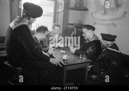 The Seven Seas Club- Life at the Merchant Navy Club, Edinburgh, Scotland, 1943 A group of seamen play cards in the bar of the Seven Seas Club in Edinburgh. Playing left to right are: Charles Stalder from the Bronx; Harry Reynolds from Pennsylvania, USA; Paul Grossman from New York; and Olaf Tier from Norway. Watching the game are: Ludvik Marum from Norway (left) and J Craamer from Holland (right). Stock Photo