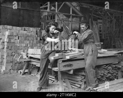 Women Carpenters Then and Now- Women at work in England, 1941 Two female carpenters drill holes for bolts in a workshop making huts, somewhere in England, 1941. The bolts will be used to join the sections of the huts together. Stock Photo