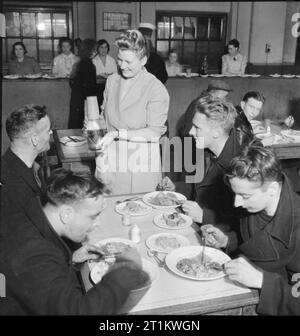 Woolmore Street Restaurant- Eating Out in Wartime London, 1942 27 year old M M Brookes (centre) brings a bottle of water to a table at which four sailors are enjoying their lunch. Clockwise from centre they are: M M Brookes (holds a diploma in domestic science and runs the restaurant), R White (21 years old, an AB), 20 year old A S Giddings (stoker), 27 year old F Cooper and 53 year old H Dowding (leading stoker). Stock Photo