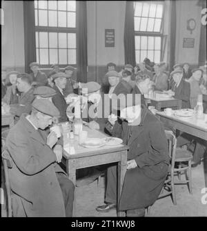 Woolmore Street Restaurant- Eating Out in Wartime London, 1942 Customers enjoy their lunchtime meal at the Woolmore Street British Restaurant in Poplar. Clockwise around the table nearest the camera are: 69 year old F Mann (a carpenter), 53 year old J Hall (demolition and iron recovery carman), 45 year old A Simmons (also working on iron recovery) and 77 year old T Hambly (served as a merchant seaman during the First World War). Many other workers can be seen at the tables in the background. Stock Photo