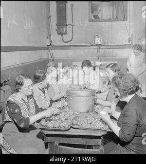 Woolmore Street Restaurant- Eating Out in Wartime London, 1942 Women at work preparing vegetables in the kitchen of the British Restaurant at Woolmore Street. Left to right they are: Mrs F Malyon (aged 59), Mrs C Pude (aged 64, a cigar worker in peacetime), Mrs Florence Skinner, Mrs Davison (once demonstrated cleaning materials), Mrs J Harrop (ran a corn chandler and grocer's store), Doris Prigge (previously in the catering trade), Miss Barkwith, Miss Violet Hancock and Mrs Turley. Another woman can be seen in the background. Stock Photo