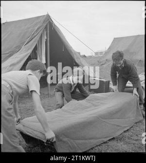 Youth Service Volunteers Help British Farmers- Agricultural Camp at Nunney Catch, Somerset, England, UK, 1943 Three boys make their beds at the Youth Service Volunteer camp at Nunney Catch, in between breakfast and work parade. Left to right, they are: Javier Sanchez (aged 16 1/2), Venanchio Zornova (aged 14) and his brother Mario Zornova (aged 16). All were refugees from the Spanish Civil War, and are on holiday from boarding school. The beds are being made outside the tents, which can be seen behind the boys as they work. Stock Photo