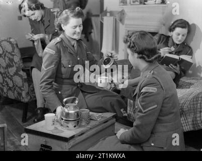 At An Ats Motor Transport Company Training Centre, Camberley, Surrey, 1941 Trainee members of the Auxiliary Territorial Service Motor Transport Company relax in the rest room at the ATS MTC Training Centre, probably at Camberley. Two women enjoy a cup of tea, whilst a third eats a biscuit as she reads, and a fourth, in the background, is sewing and appears to be darning a sock. Stock Photo