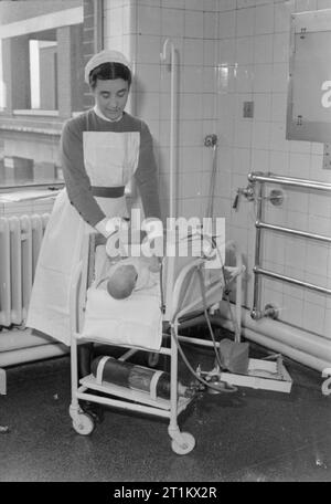 Baby's Life Saving Cot Designed by Nurse at Middlesex Hospital, London, England, UK, 1945 Sister Mary Williams places a young baby into the new cot she has designed at Middlesex Hospital, London. The cot is a 'box' on a stand and is leaning at a 45 degree angle: it can be laid flat. An oxygen cannister can be seen on the lower part of the frame. The ends of the cot are removable so that the baby can be treated without being lifted out. Stock Photo