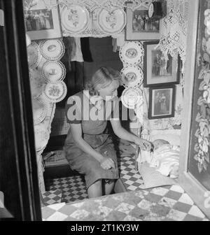 British Canals in Wartime- Transport in Britain, 1944 A mother settles her baby down to sleep in the cabin of her canal boat. The cabin is adorned with decorative plates, family photographs and lace, which, according to the original caption 'are the hallmarks of a good canal boat cabin'. Stock Photo