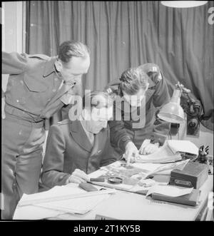 British Equipment at An American Airfield- Anglo-american Co-operation in Wartime Britain, 1943 Intelligence officers examine aerial photographs taken during a raid on Huls. Left to right, they are: Captain Joseph R Harmon from Chicago; Major Gardiner H Fiske from Boston, Massachusetts; and Captain Ira E Wight from St Louis, Missouri. All office furniture has been supplied by Britain under the 'reverse Lease-Lend' scheme. Stock Photo