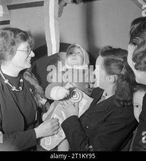 Bwrs Christmas Gifts Distributed To London's East Enders- American Aid To the Canning Town Settlement, London, England, UK, December 1944 Miss Constance Holland (left), warden of Canning Town settlement, helps Mrs R Myner of Plaistow to choose a toy for her two year old son William Charles from the selection of gifts donated by America. William appears to be fascinated by the paper streamers which decorate the room! Stock Photo