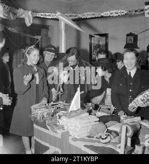 Bwrs Christmas Gifts Distributed To London's East Enders- American Aid To the Canning Town Settlement, London, England, UK, December 1944 Miss Constance Holland, the warden of Canning Town settlement, (centre) helps Norma Terry and Doreen Jones (left) to choose a gift from the pile of American toys on the table in front of them. The room is decorated with paper streamers and a member of the Women's Voluntary Service (WVS) can be seen between Doreen and Norma. The girls are both from Plaistow. Stock Photo