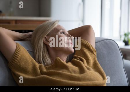 Happy peaceful middle aged lady relaxing on home sofa Stock Photo