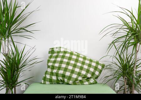 An empty bed with a green pillow and palm trees on the sides against a white wall. Place for text. Stock Photo