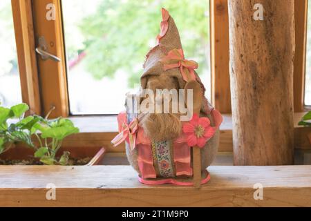 Easter bunny doll in a hat on a wooden shelf in front of the window. Stock Photo